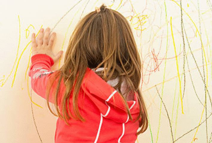 une petite fille dessine sur un mur peint