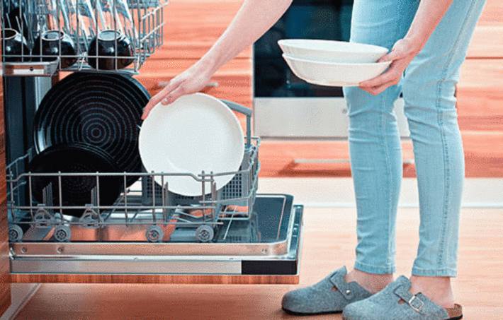 une femme en pantalon turquoise sort des assiettes du lave vaisselle