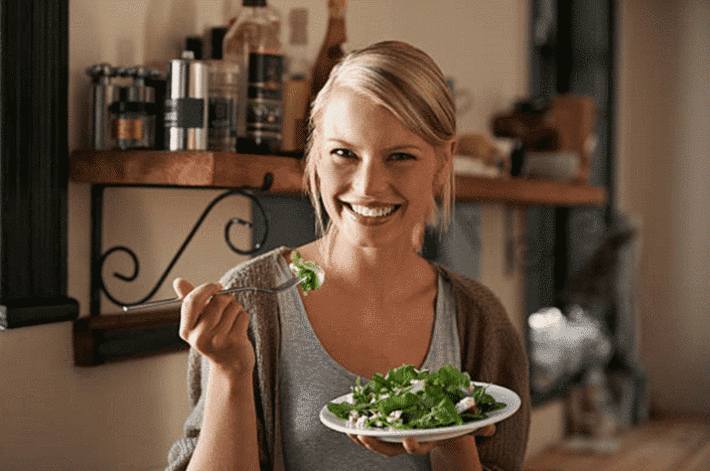 femme-blonde-souriante-mangeant-de-la-salade-verte.