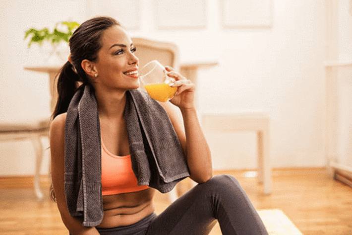 jeune-femme-brune-assise-en tenue-de-sport-tenant-un-verre-de-jus-d-orange